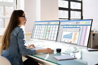 Accounting professional reviewing financial and tax reporting data on dual monitors during the transition from FIRE to IRIS for oil and gas information return filing.
